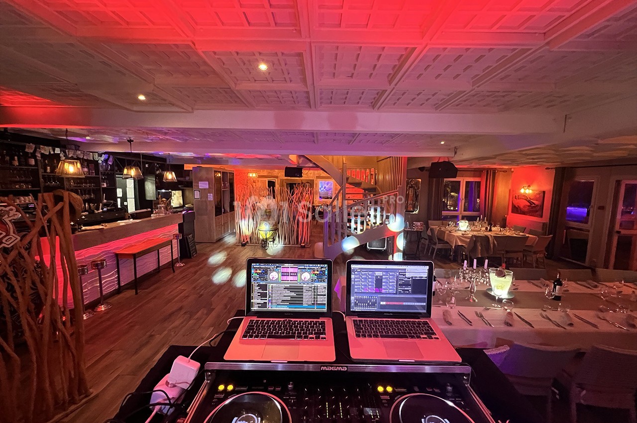 Vue depuis une table de mixage sur une salle de réception éclairée de lumières rouges et décorée pour un événement.