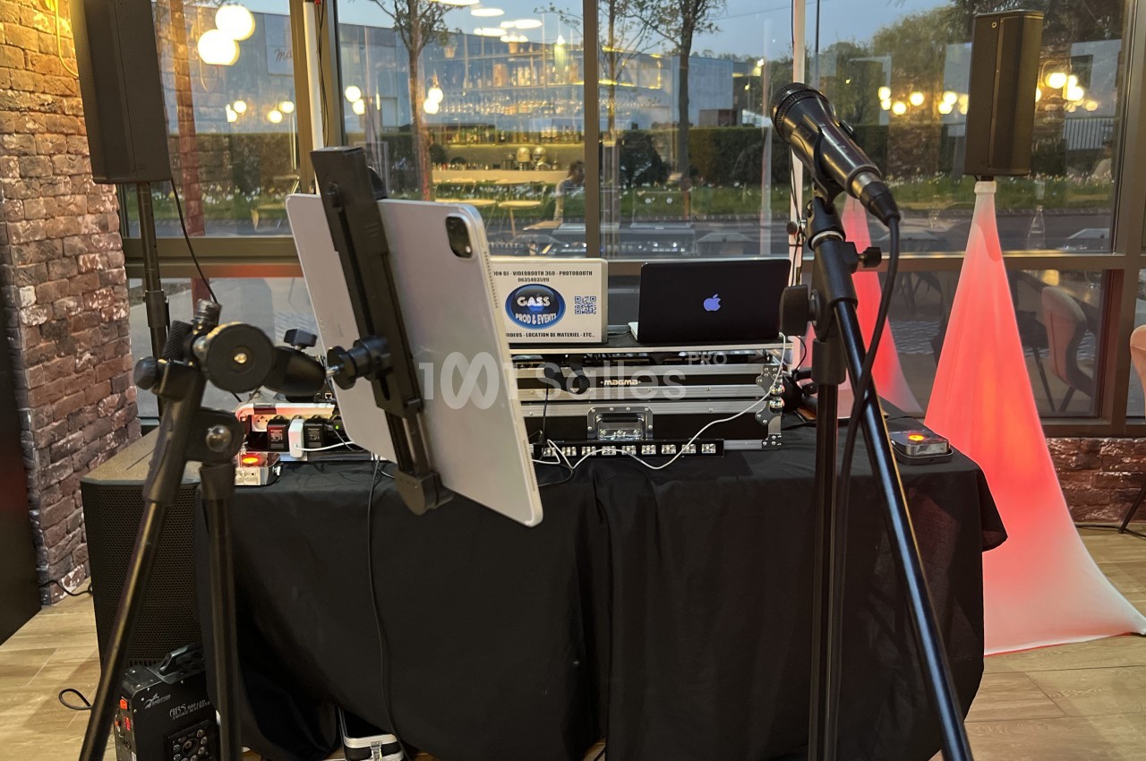 Équipement de DJ installé avec table de mixage, ordinateur, tablette et micros dans un espace intérieur vitré.