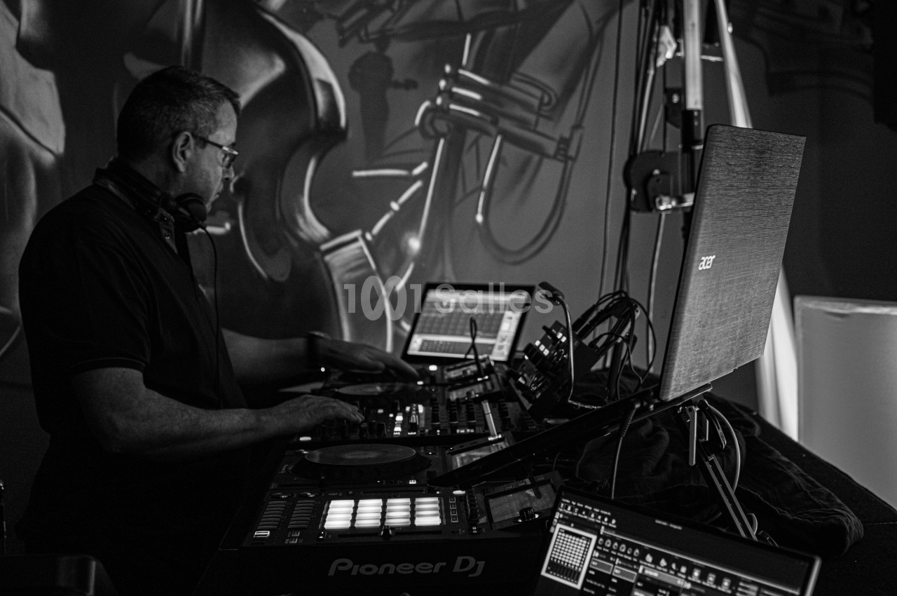 Un DJ mixe de la musique sur une table de mixage entourée d'équipements électroniques dans un studio sombre.