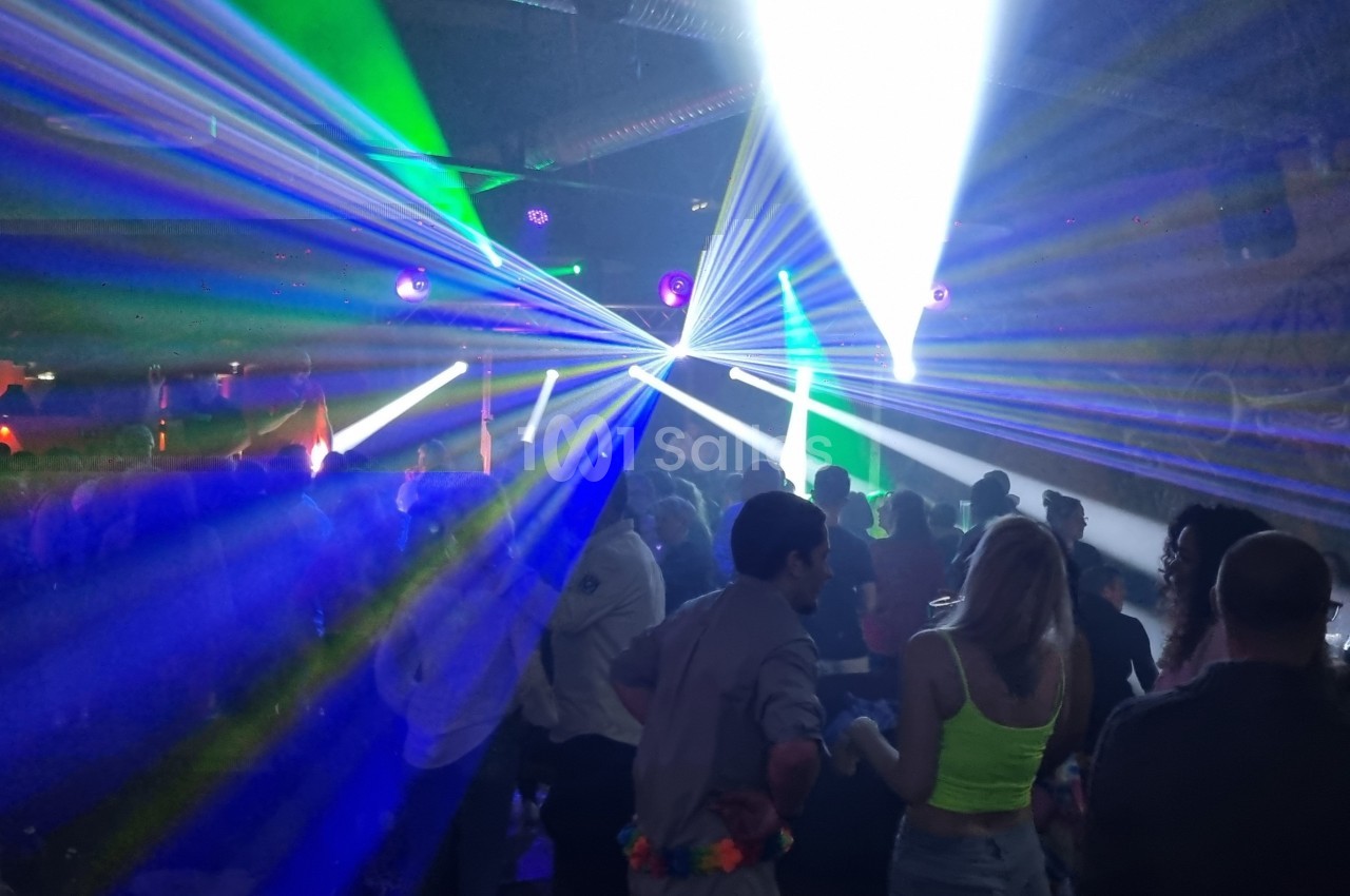Des personnes dansent dans une salle sombre illuminée par des faisceaux lumineux colorés et des projecteurs.