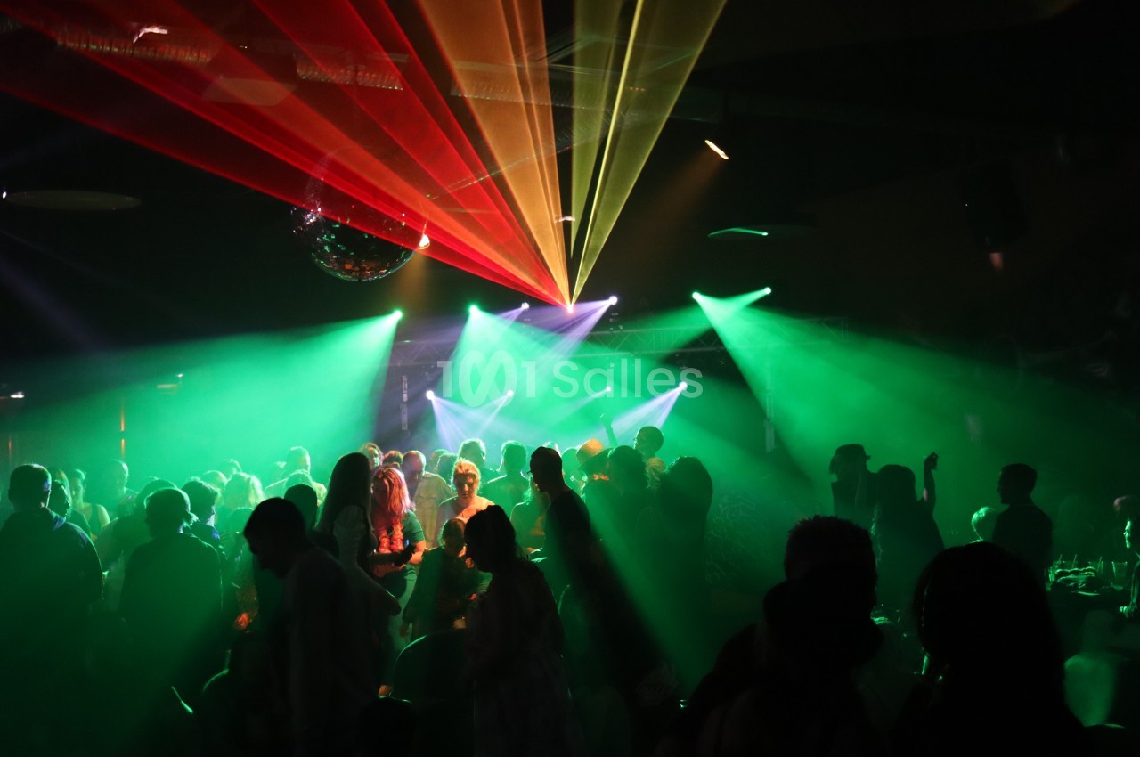 Des personnes dansent sous des lumières colorées et des faisceaux laser dans une ambiance festive.