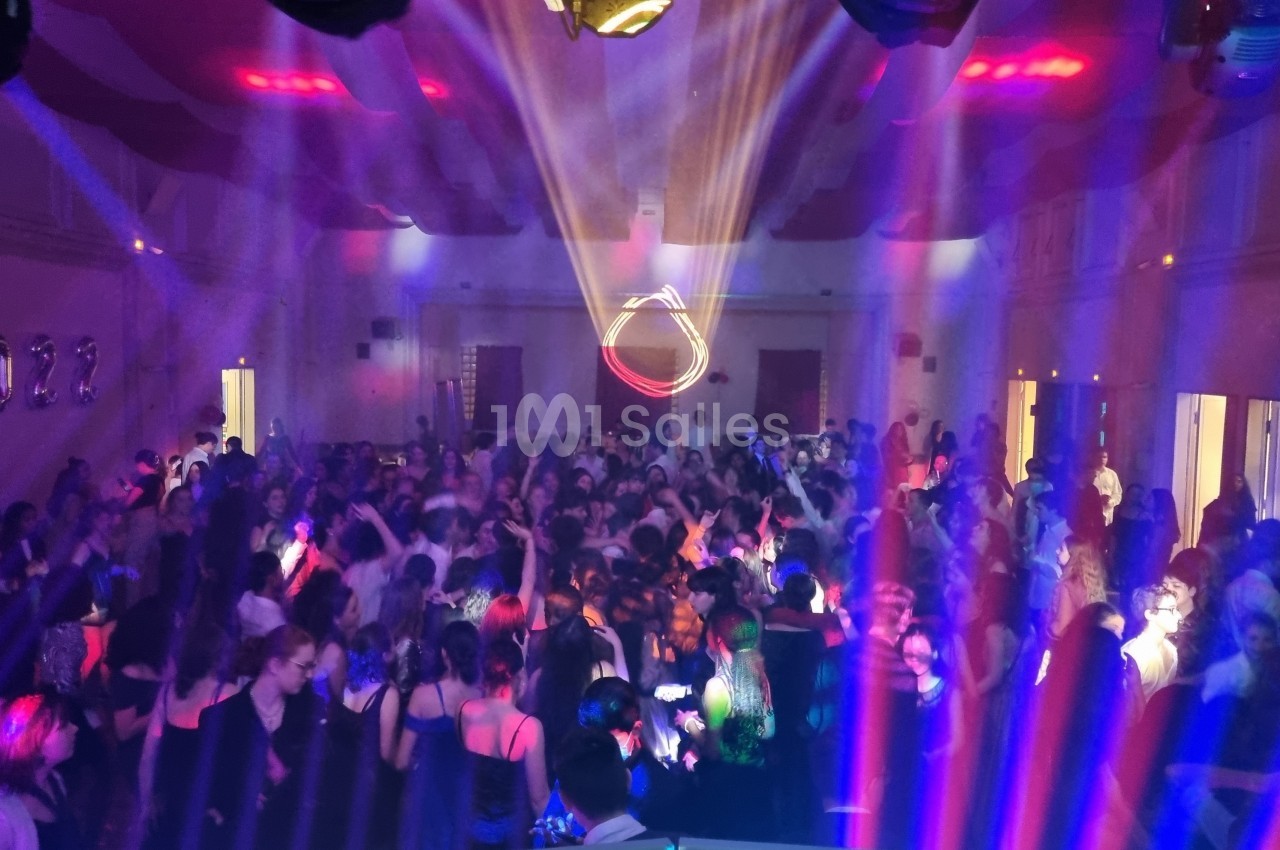 Salle comble avec des personnes dansant sous des lumières colorées et des décorations marquées ’2023’.