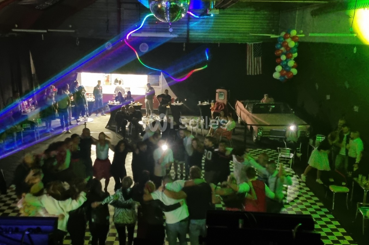 Groupe de personnes dansant sous des lumières colorées dans une salle décorée avec des ballons et une piste en damier.