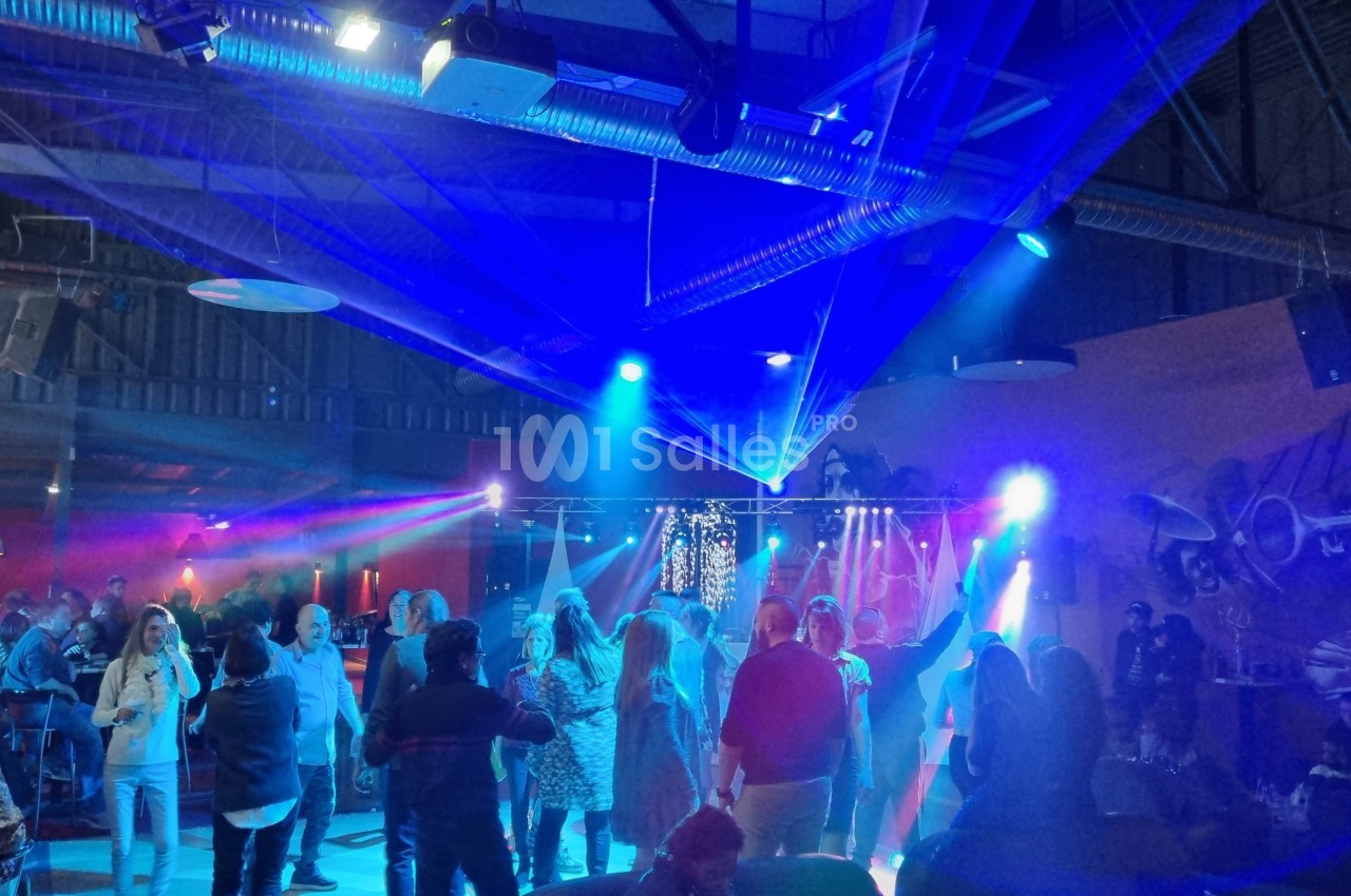 Des personnes dansent sous des lumières colorées dans une salle avec un plafond industriel et des projecteurs.