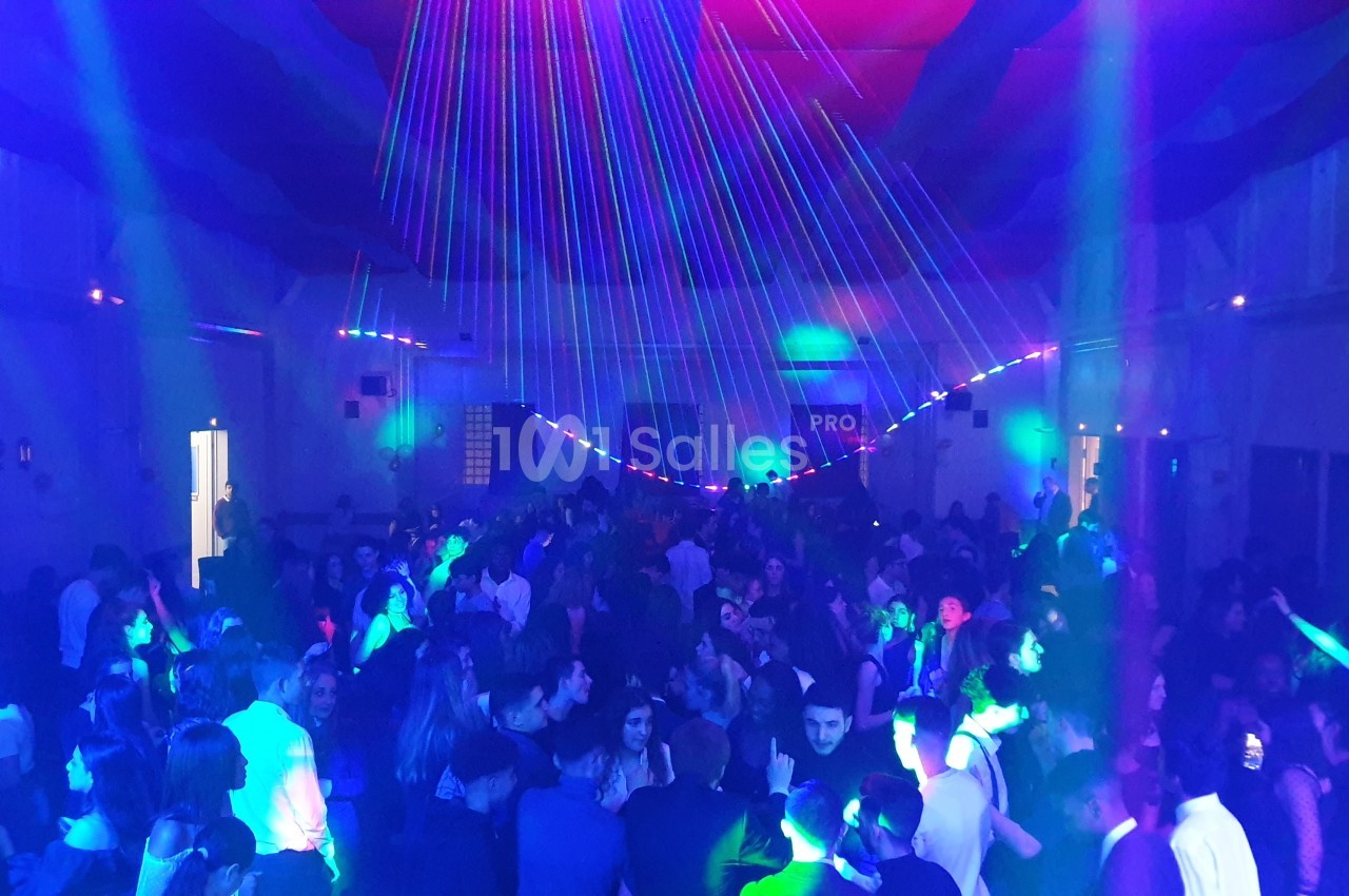 Foule dans une salle illuminée par des jeux de lumière colorés lors d'une soirée festive.