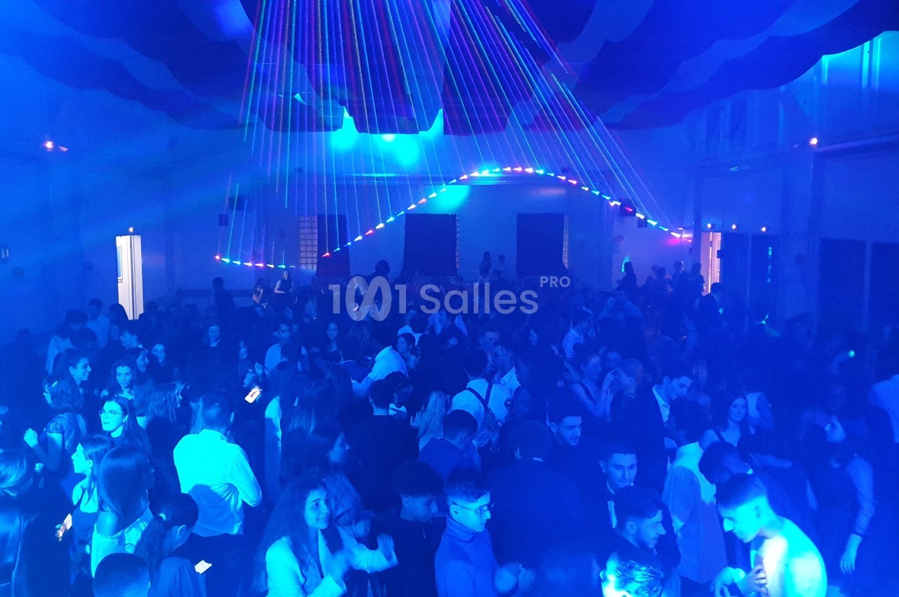Salle remplie de personnes dansant sous des lumières colorées et des faisceaux laser dans une ambiance festive.