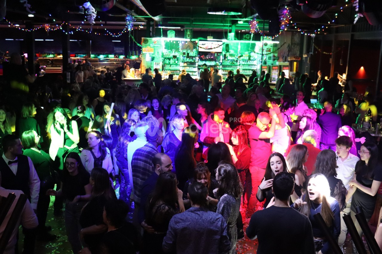 Personnes dansant et socialisant dans une salle de fête éclairée par des lumières colorées et décorée de guirlandes.