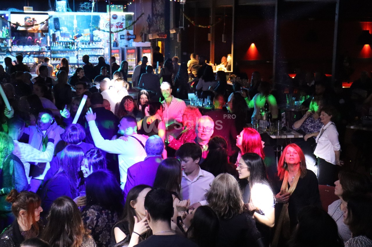 Groupe de personnes dans une ambiance festive avec éclairages colorés, dans un bar ou une salle animée.
