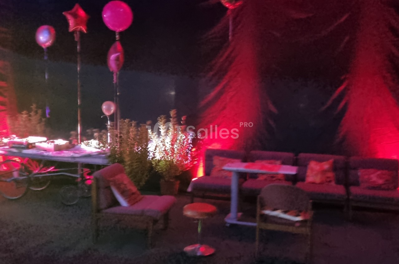 Espace lounge décoré avec des ballons, des canapés et un éclairage rouge dans une ambiance festive.