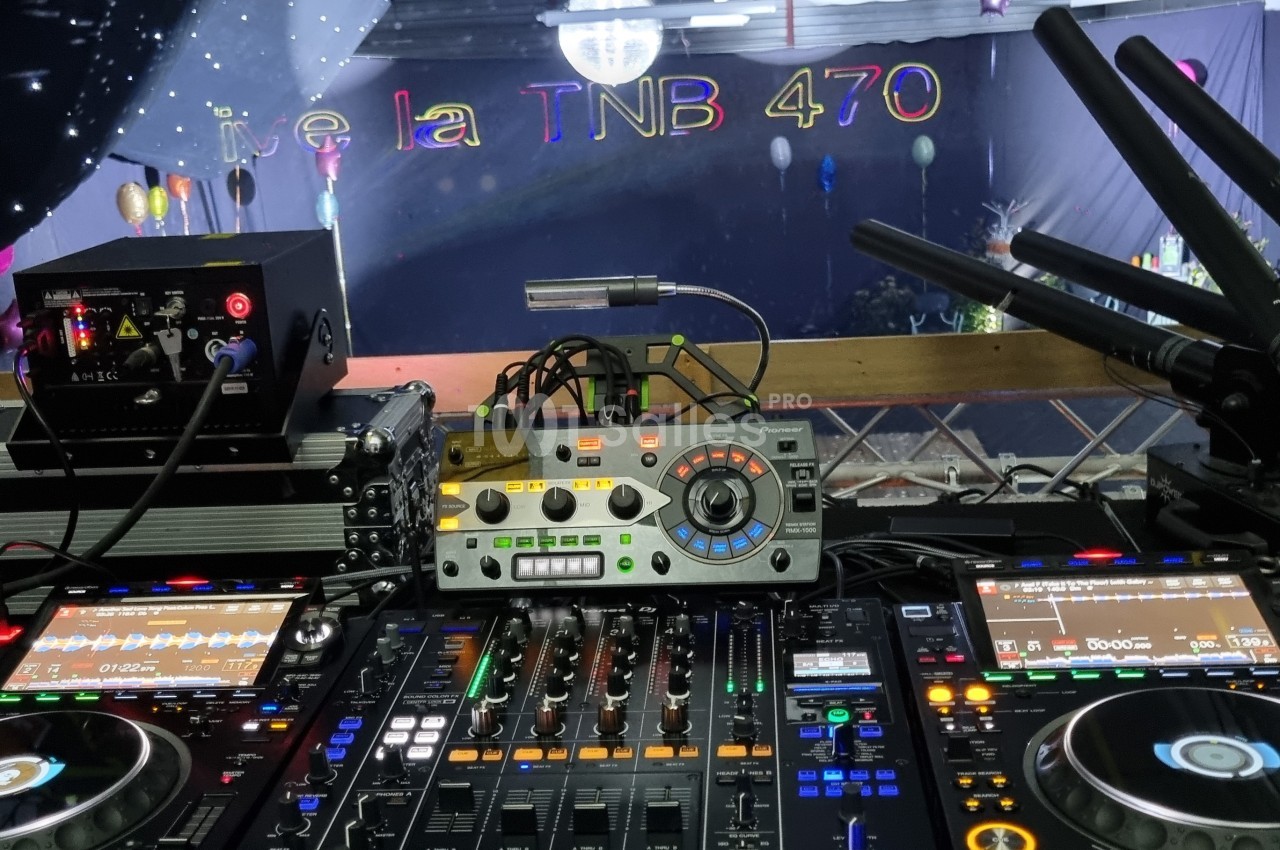 Vue d'une table de mixage DJ avec platines et équipements audio, éclairée dans une salle décorée pour un événement.