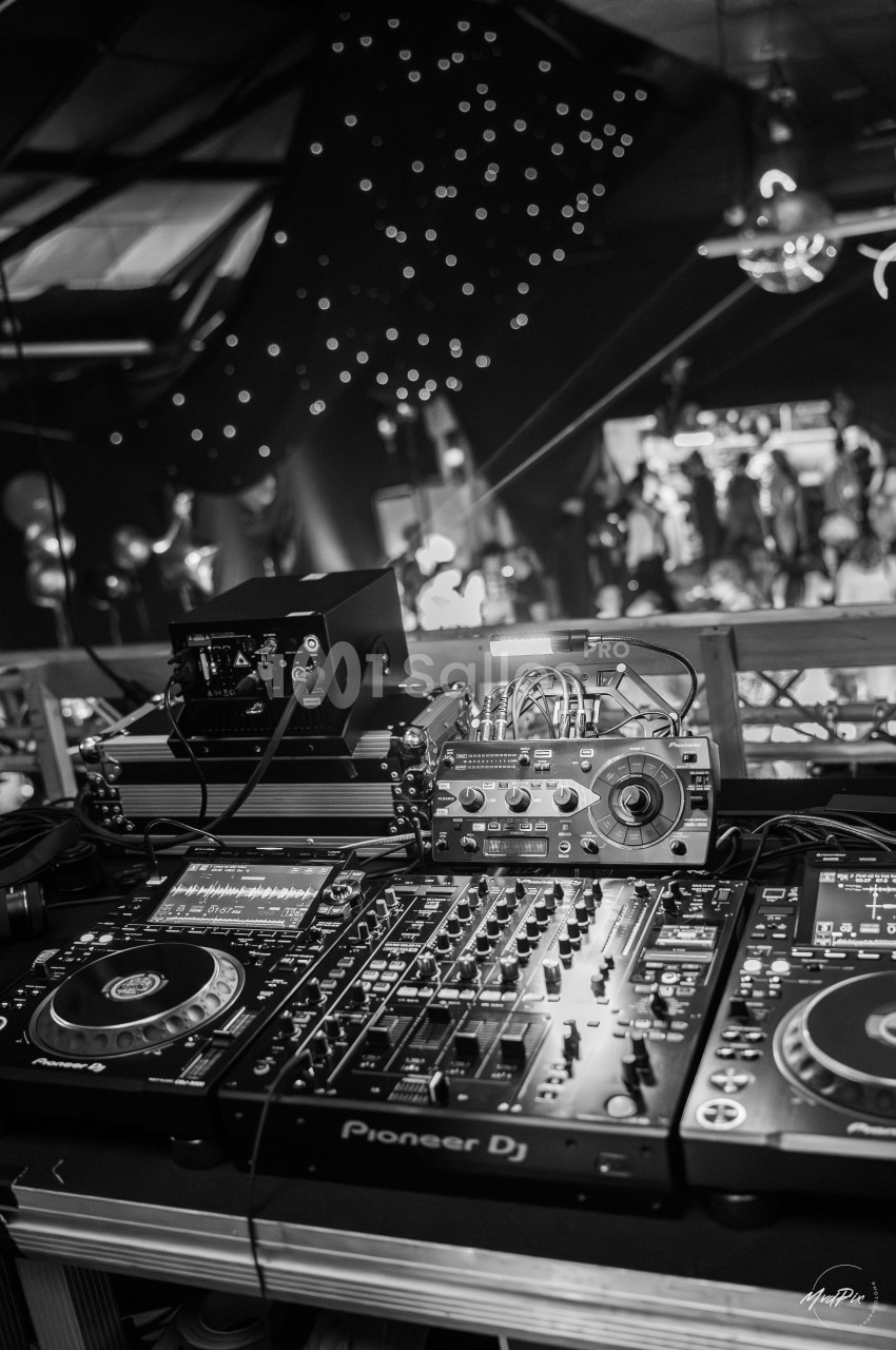 Console de mixage DJ avec platines et équipements audio dans une ambiance de fête sous des lumières tamisées.