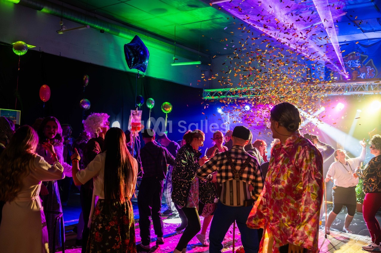 Groupe de personnes dansant sous des lumières colorées avec des confettis tombant dans une ambiance festive.