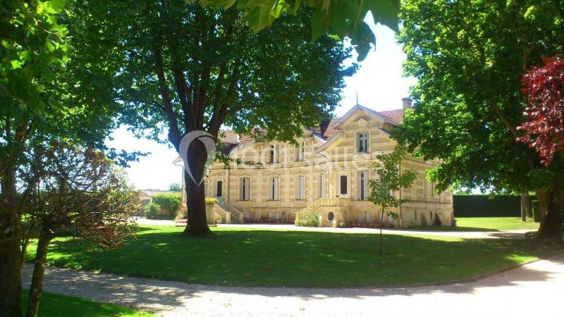 Manoir en pierre entouré d'arbres et de pelouses, avec un chemin gravillonné au premier plan.