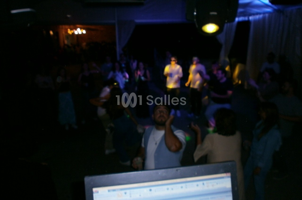 Groupe de personnes dansant dans une ambiance sombre avec éclairage coloré, vu depuis une table de mixage.