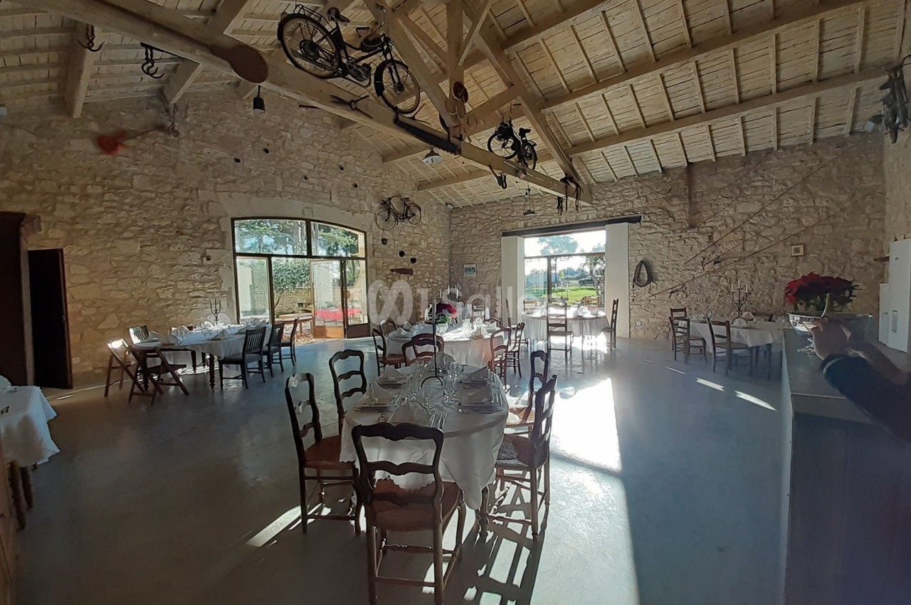Salle lumineuse avec murs en pierre, tables dressées, poutres apparentes et vélos suspendus au plafond.