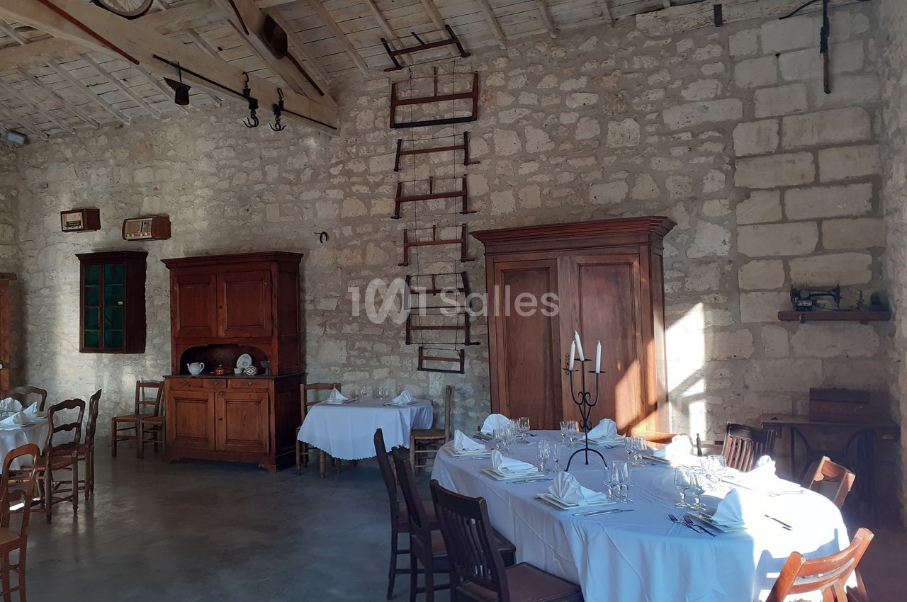 Salle à manger rustique avec murs en pierre, meubles en bois, tables dressées et lumière naturelle.