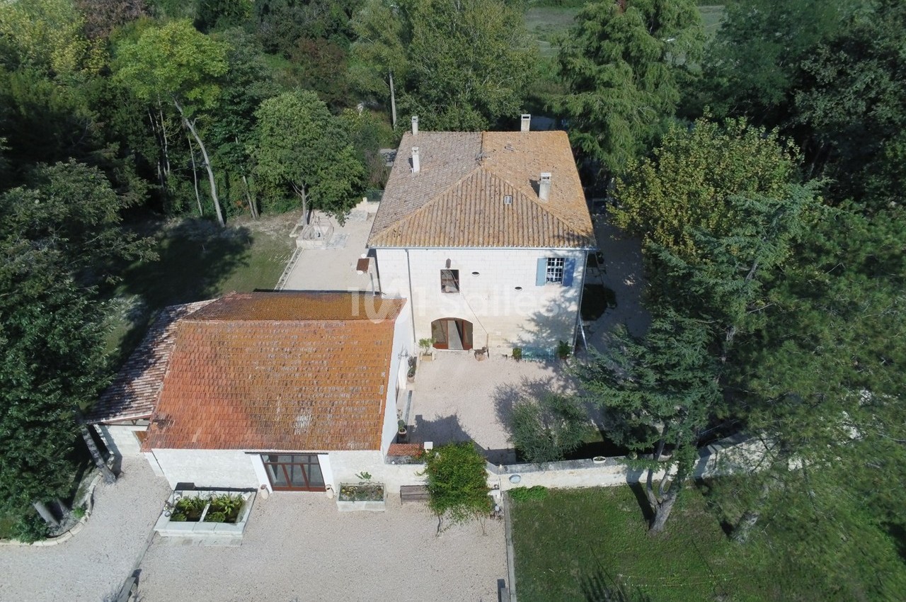 Vue aérienne d'une maison en pierre avec toit en tuiles, entourée d'arbres et d'une cour gravillonnée.