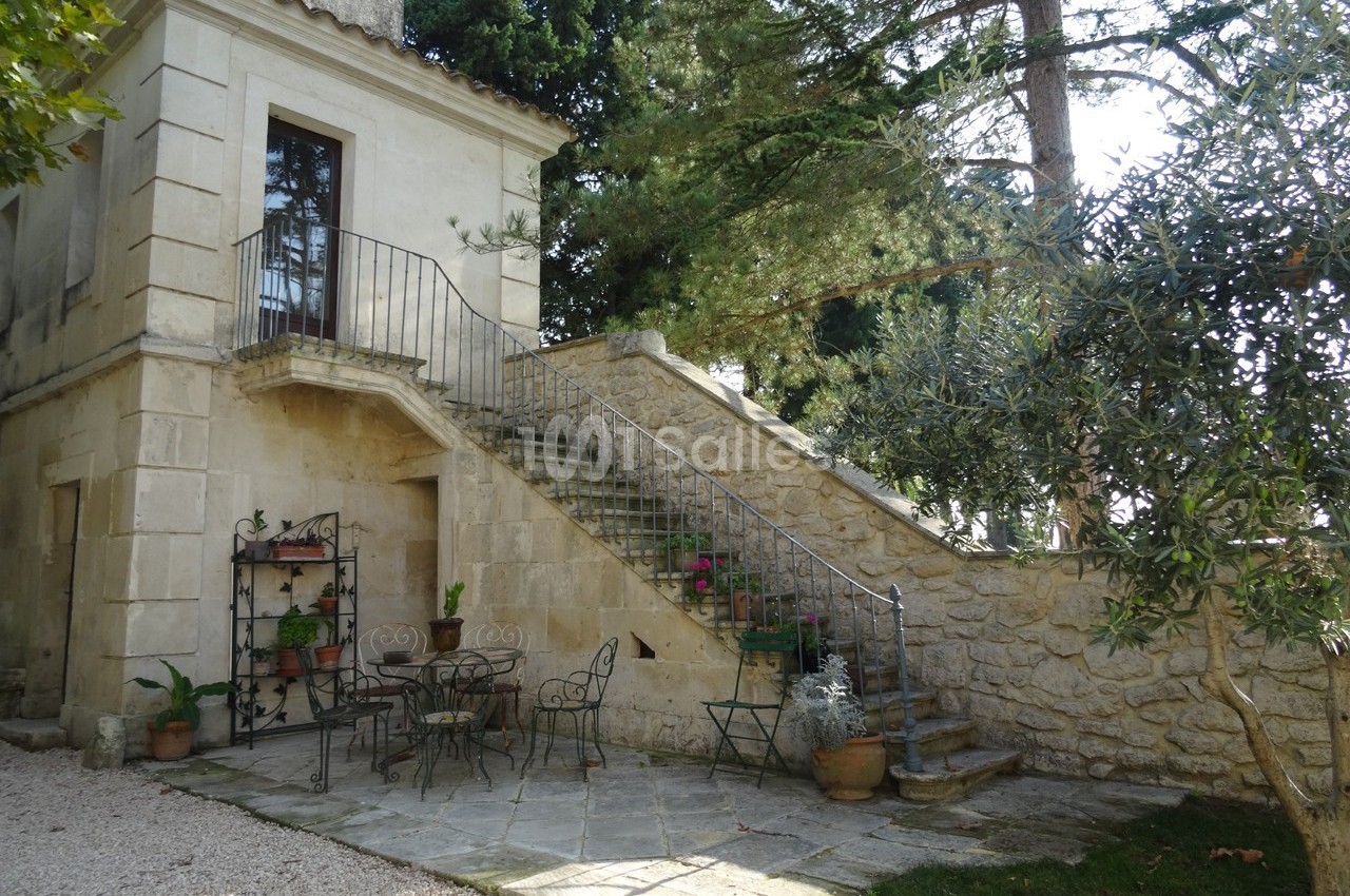 Escalier extérieur en pierre menant à une porte, avec terrasse aménagée de mobilier en fer forgé et plantes en pot.