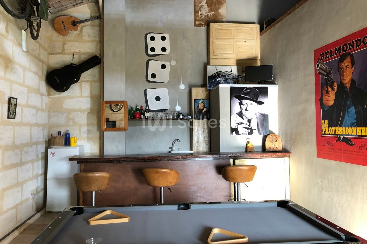 Bar aménagé avec un billard, des tabourets, des décorations murales variées et une affiche de film rétro.