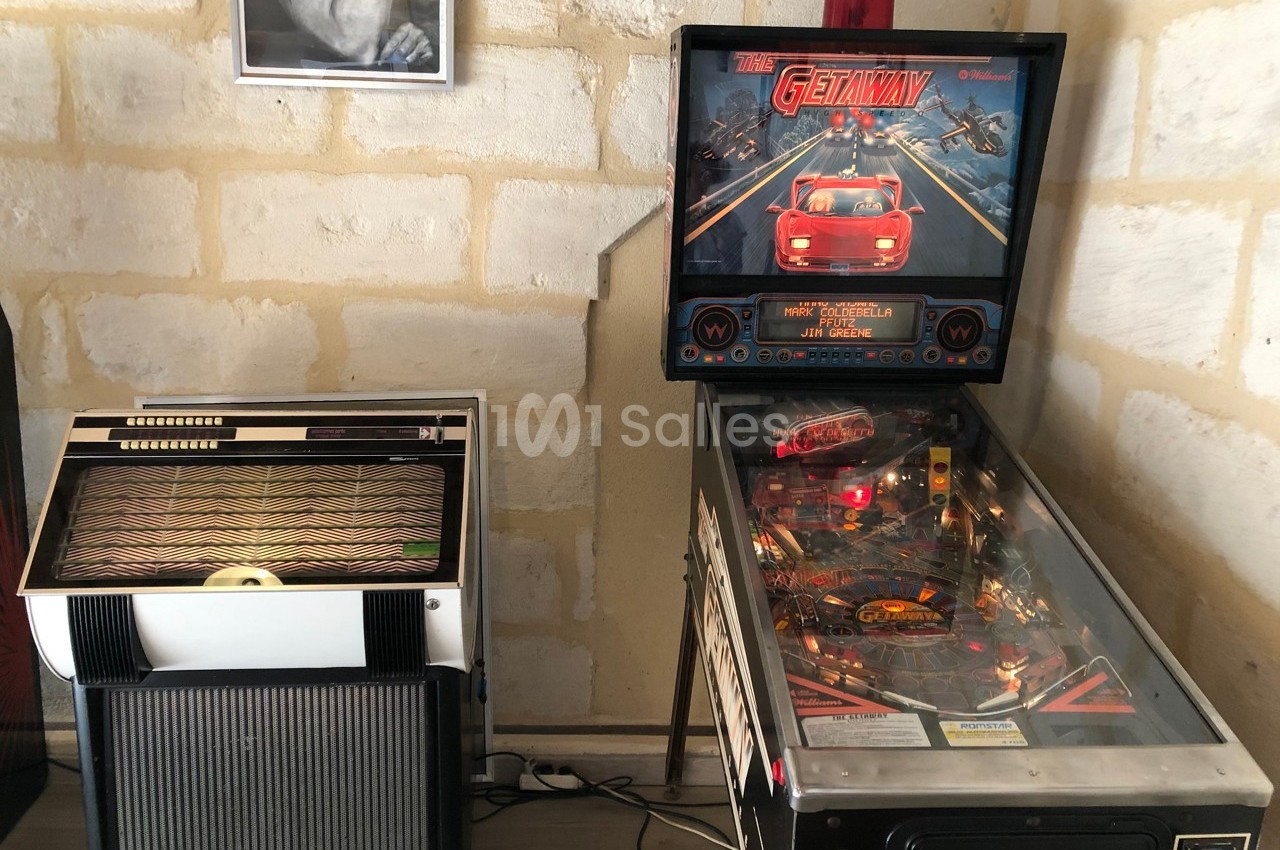 Un flipper et un jukebox vintage placés côte à côte dans une pièce aux murs en pierre.