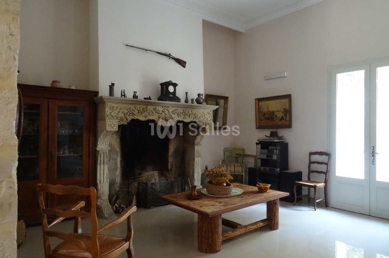 Salon avec cheminée en pierre sculptée, meubles en bois, armoire vitrée, et décoration murale rustique.