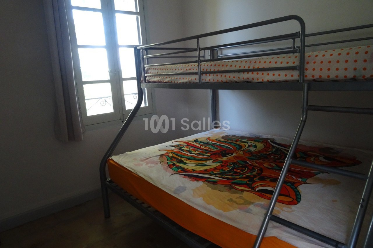 Lit superposé en métal dans une chambre lumineuse avec une fenêtre et une couverture colorée sur le lit inférieur.