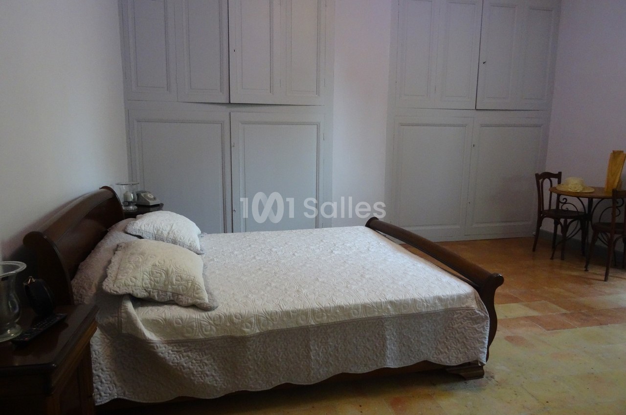 Chambre avec un lit double en bois, draps blancs, armoires encastrées et table avec chaises dans un coin.
