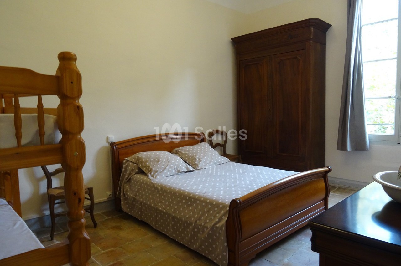 Chambre avec lit double, lits superposés en bois, armoire ancienne et fenêtre laissant entrer la lumière naturelle.