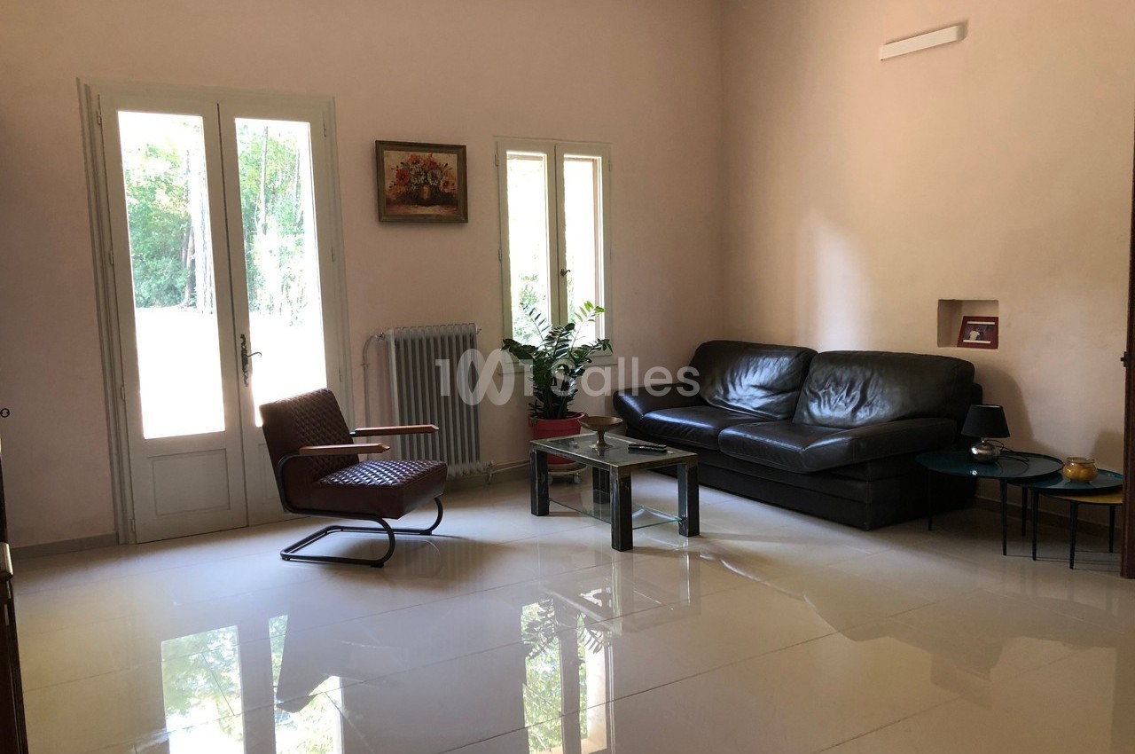 Salon lumineux avec canapé en cuir noir, fauteuil, table basse en verre et vue sur un jardin par une porte vitrée.