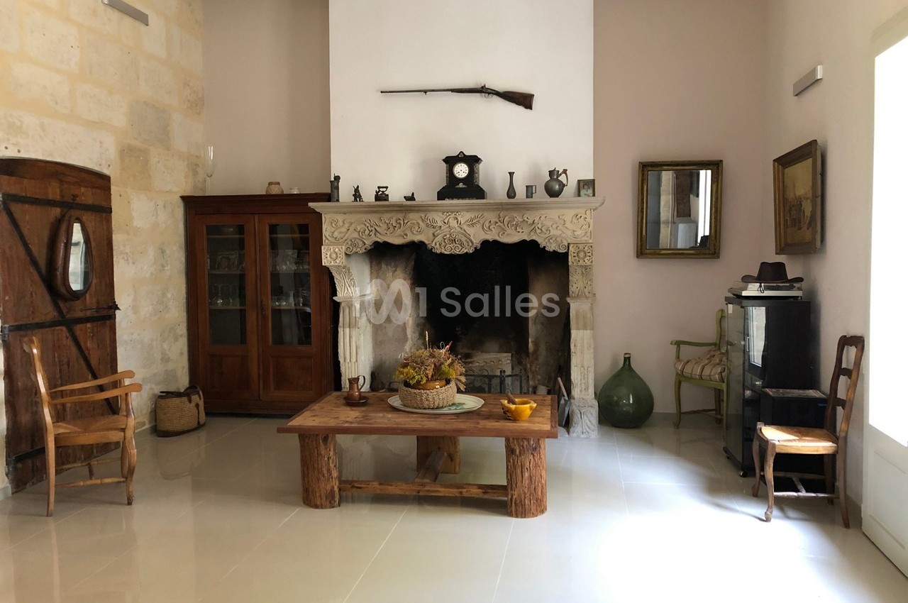 Salon rustique avec cheminée en pierre sculptée, mobilier en bois, objets décoratifs et lumière naturelle.