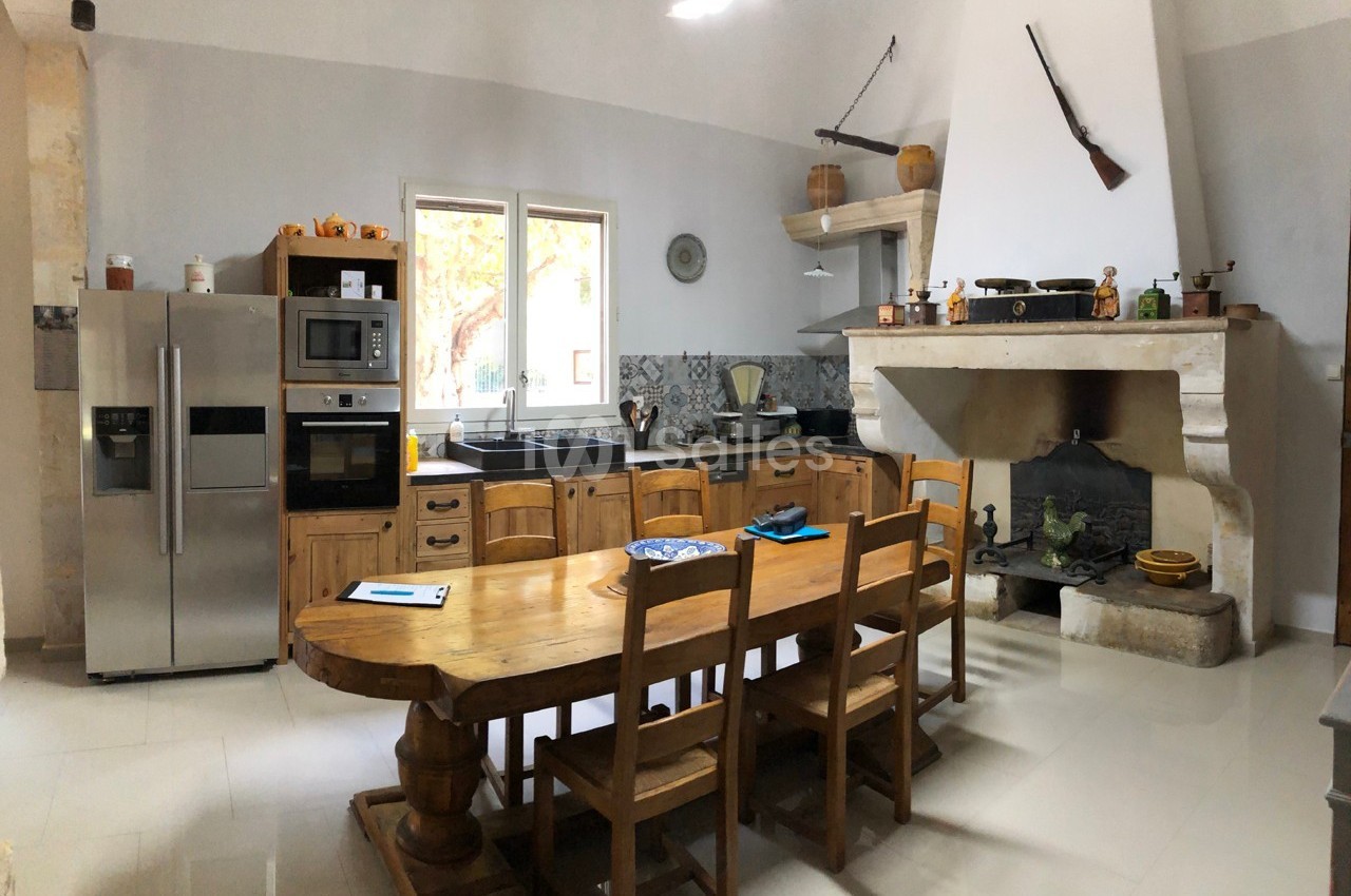 Cuisine rustique avec table en bois, cheminée ancienne, électroménagers modernes et fenêtres donnant sur l'extérieur.