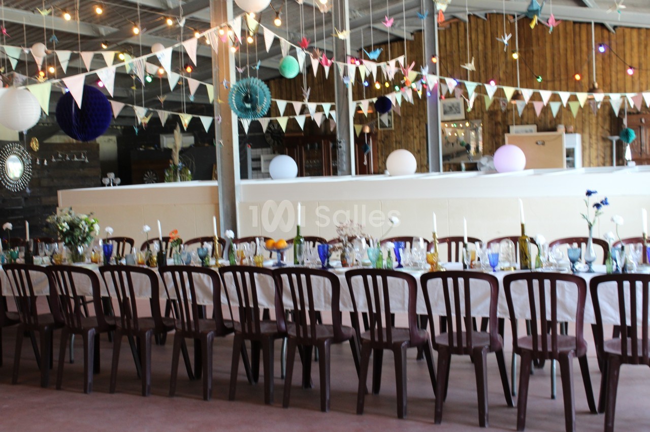 Salle décorée pour un événement avec une longue table dressée, des guirlandes lumineuses et des fanions suspendus.