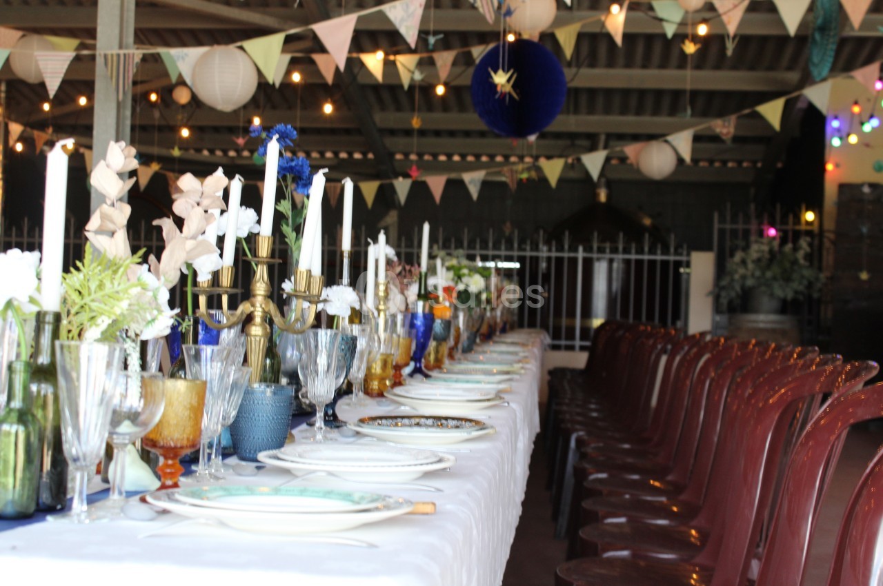 Table décorée pour un repas festif, avec chandeliers, vaisselle colorée et guirlandes suspendues en arrière-plan.