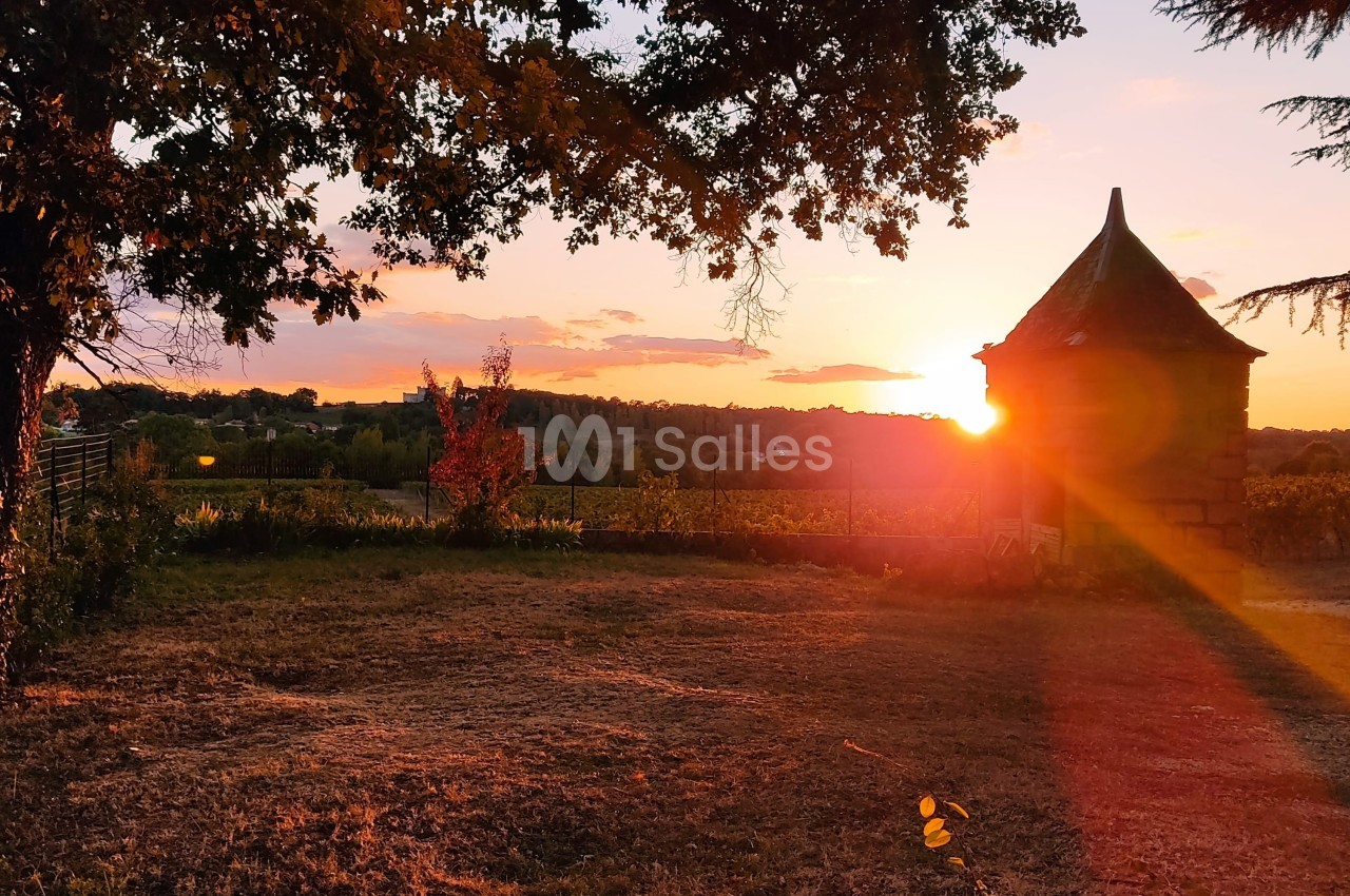 Coucher de soleil illuminant un jardin avec un petit bâtiment en pierre et des arbres en arrière-plan.
