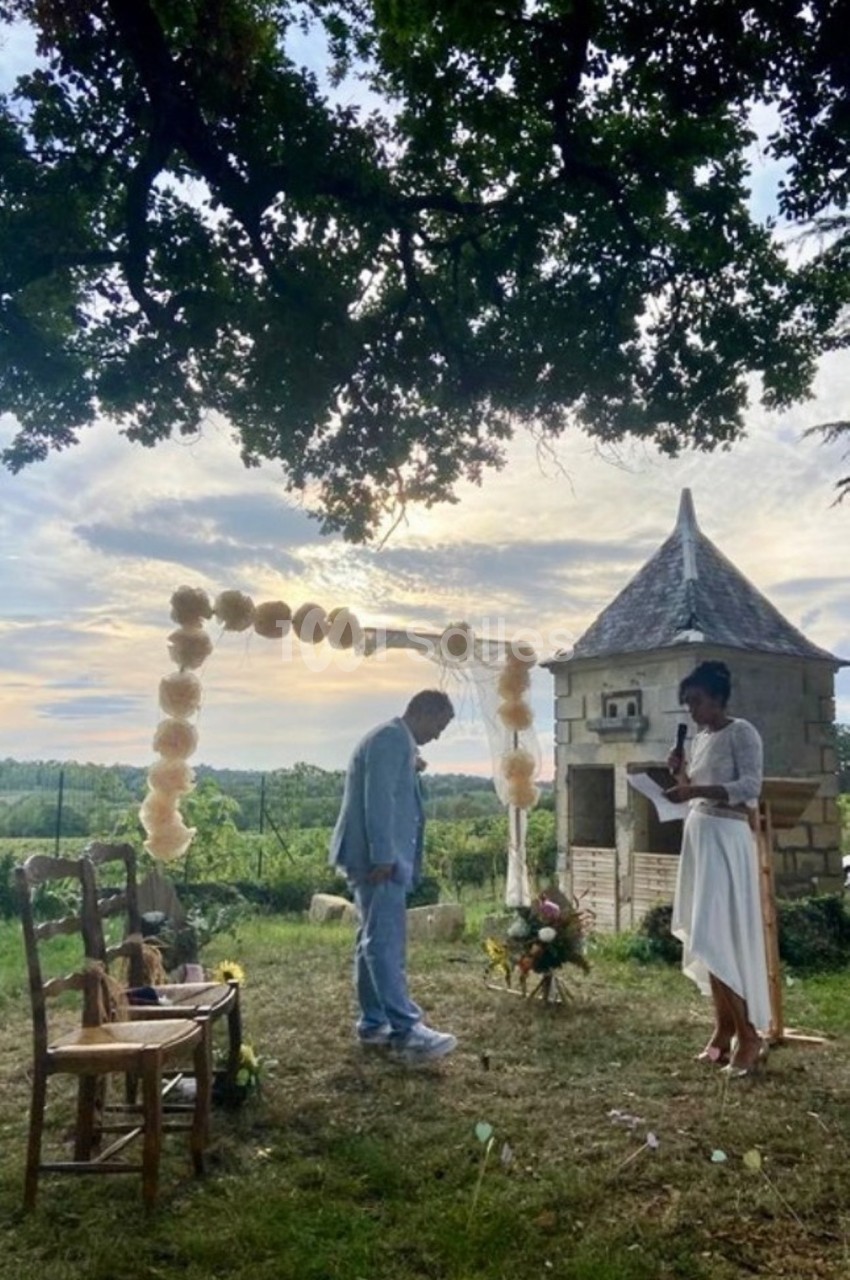Un couple échange des vœux sous une arche décorée de fleurs dans un jardin au coucher du soleil.