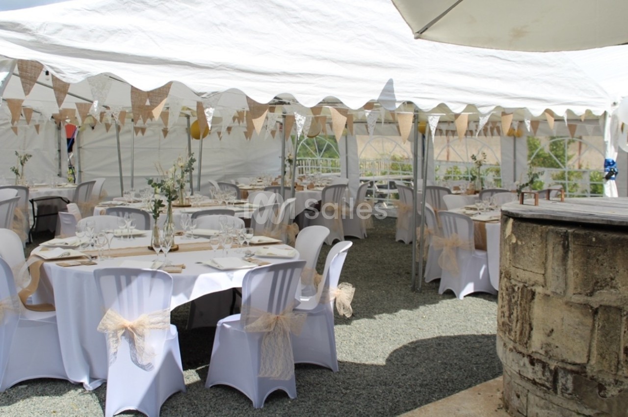 Tables décorées sous une tente blanche avec nappes, chaises ornées de rubans et guirlandes en toile de jute.