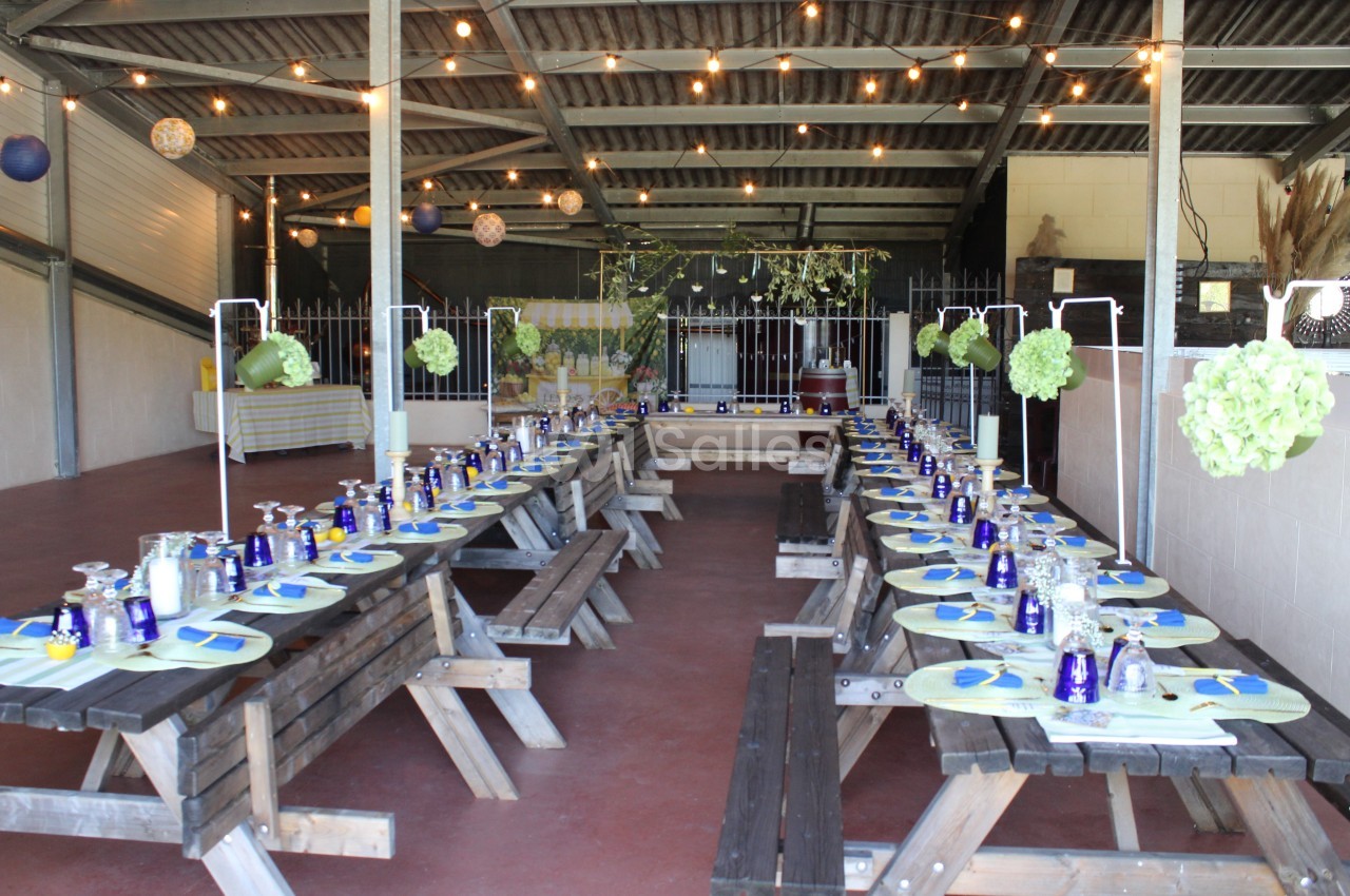 Tables en bois alignées dans une salle décorée avec des guirlandes lumineuses et des éléments floraux suspendus.