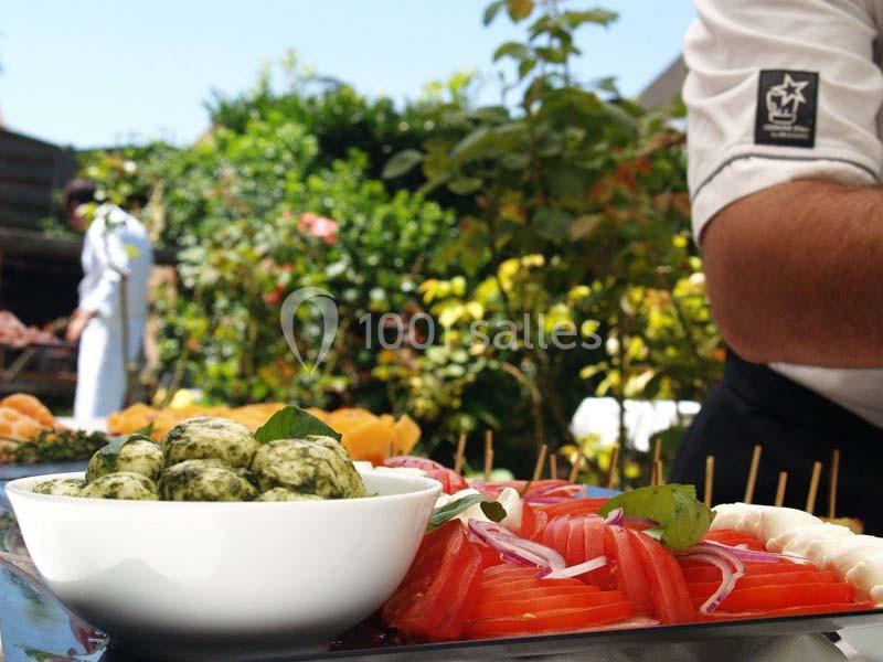 Assiette de légumes frais et brochettes, avec un bol de boules vertes, présentée en extérieur sous un ciel ensoleillé.