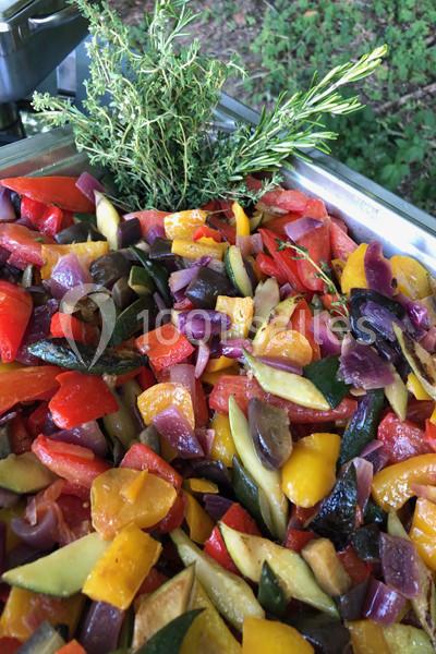 Légumes colorés coupés en morceaux et cuits, garnis de branches de thym et de romarin, présentés dans un plat.