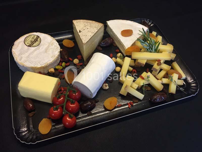 Plateau de fromages variés avec fruits secs, tomates cerises et herbes, présenté sur une nappe noire.