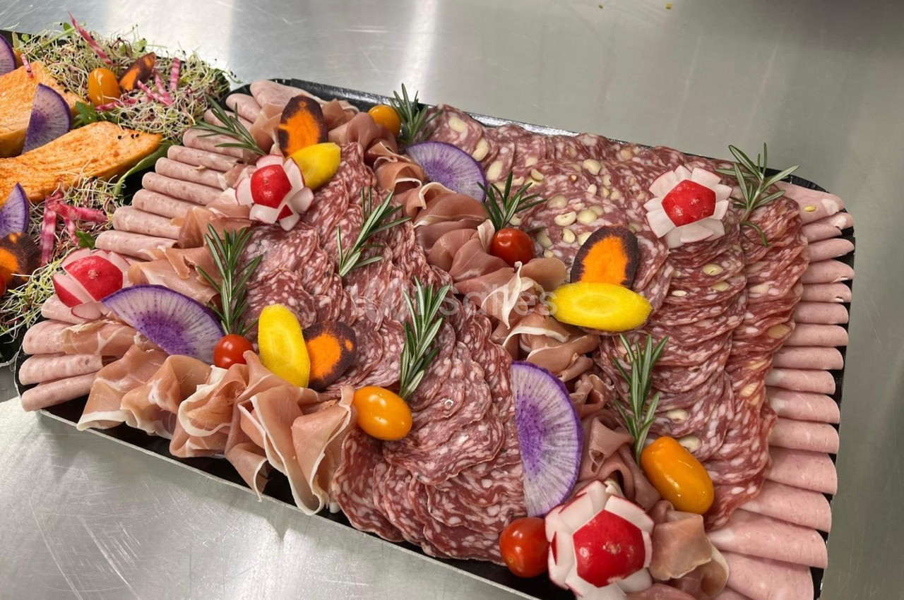 Plateau de charcuterie avec tranches de saucisson, jambon, légumes colorés et décorations de romarin.
