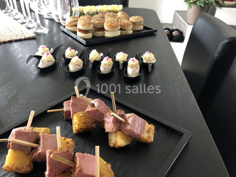 Plateau de bouchées apéritives variées disposées sur une table noire, incluant viande, ananas, mini-burgers et verrines.