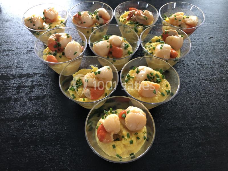 Verrines de purée jaune garnies de noix de Saint-Jacques et de ciboulette sur une table noire.