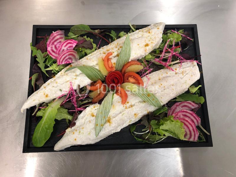 Filets de poisson cuits présentés sur un lit de salade verte, betteraves tranchées et décoration de légumes colorés.