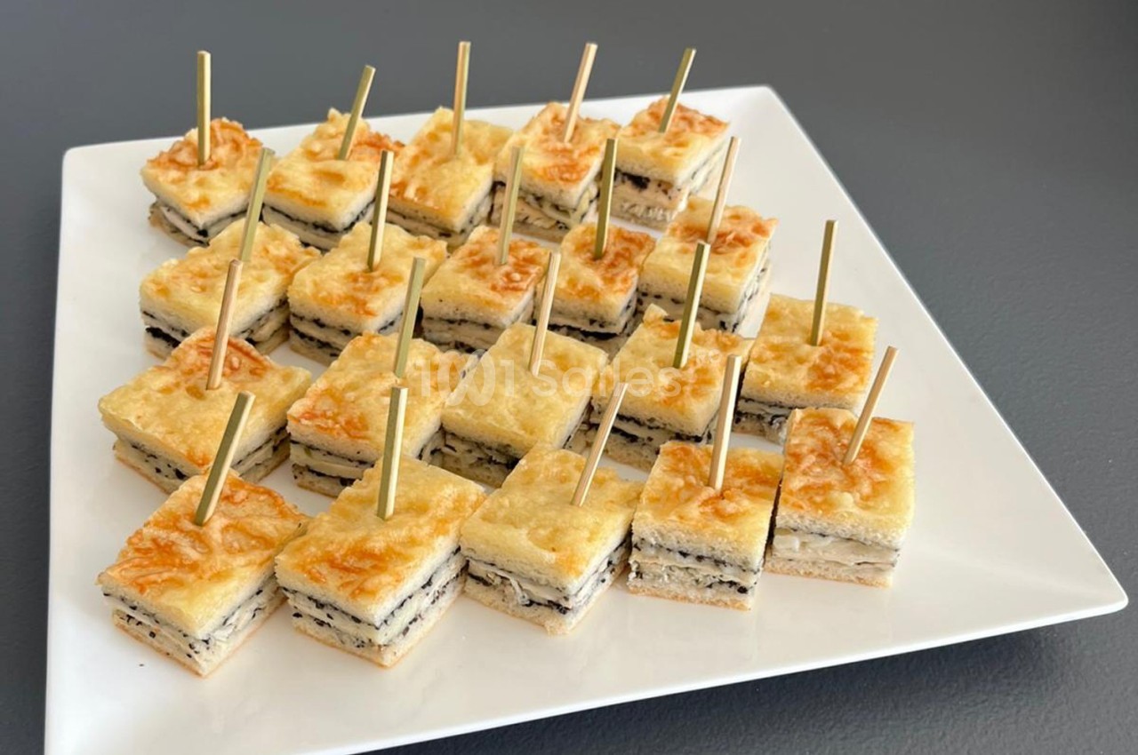 Carrés de croque-monsieur garnis de fromage et truffe, présentés sur un plateau blanc avec des piques en bois.