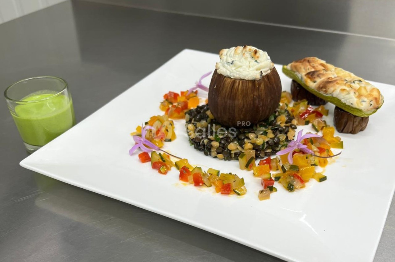 Assiette gastronomique avec aubergine farcie, lentilles, légumes colorés, pain garni et verrine de soupe verte.