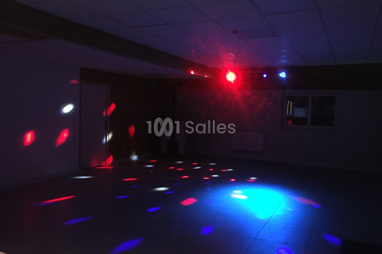 Salle sombre avec des lumières colorées projetées au sol et au mur, créant une ambiance festive.