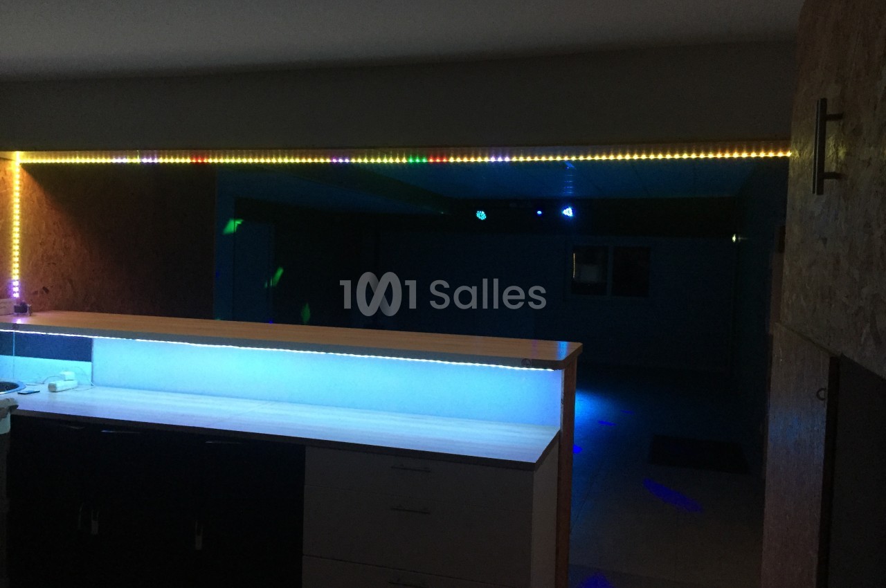 Plan de travail éclairé par des LED colorées dans une pièce sombre avec un mur en bois et un espace ouvert en arrière-plan.