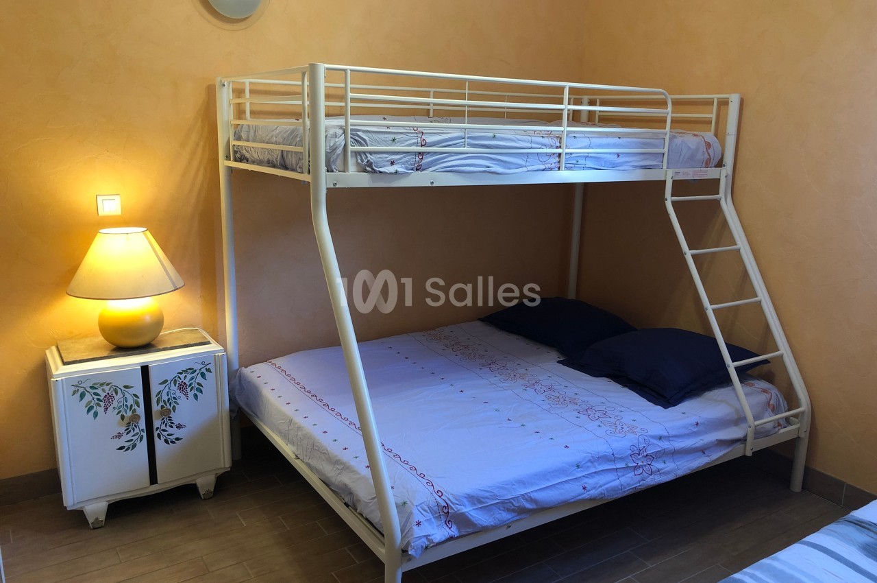 Lit superposé avec un lit double en bas et un lit simple en haut, dans une chambre aux murs orange avec une lampe de chevet.