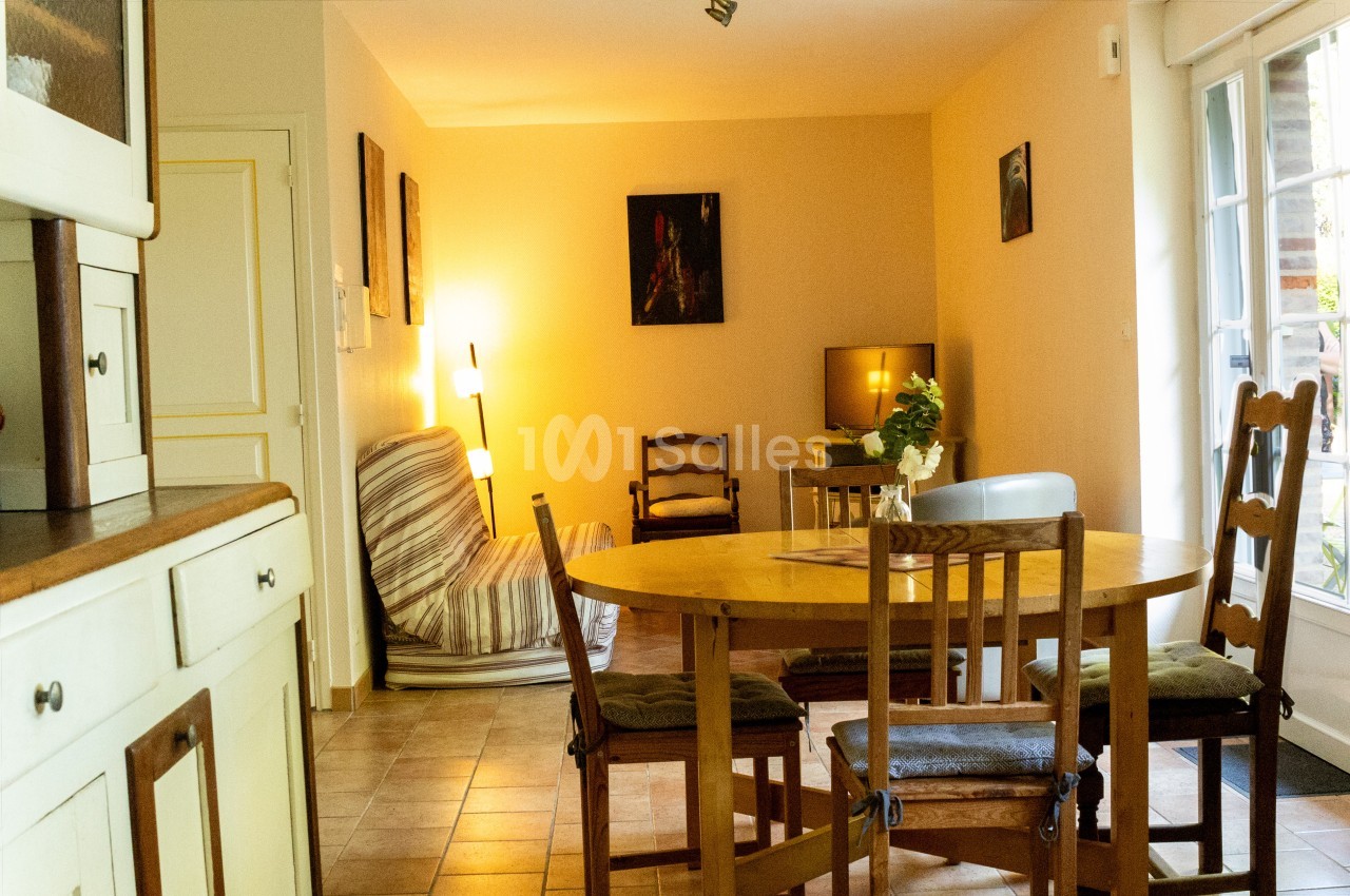 Salle à manger lumineuse avec table en bois, chaises, canapé, lampadaire et vue sur une porte-fenêtre donnant sur l…